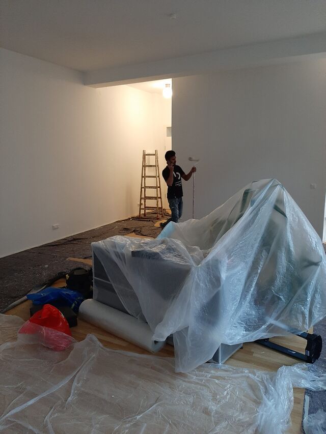 Zimmer mit Möbeln unter Folie, im Hintergrund arbeitet ein Handwerker an der Wand