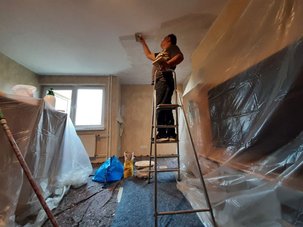 Handwerker auf einer Leiter spachtelt die Zimmerdecke