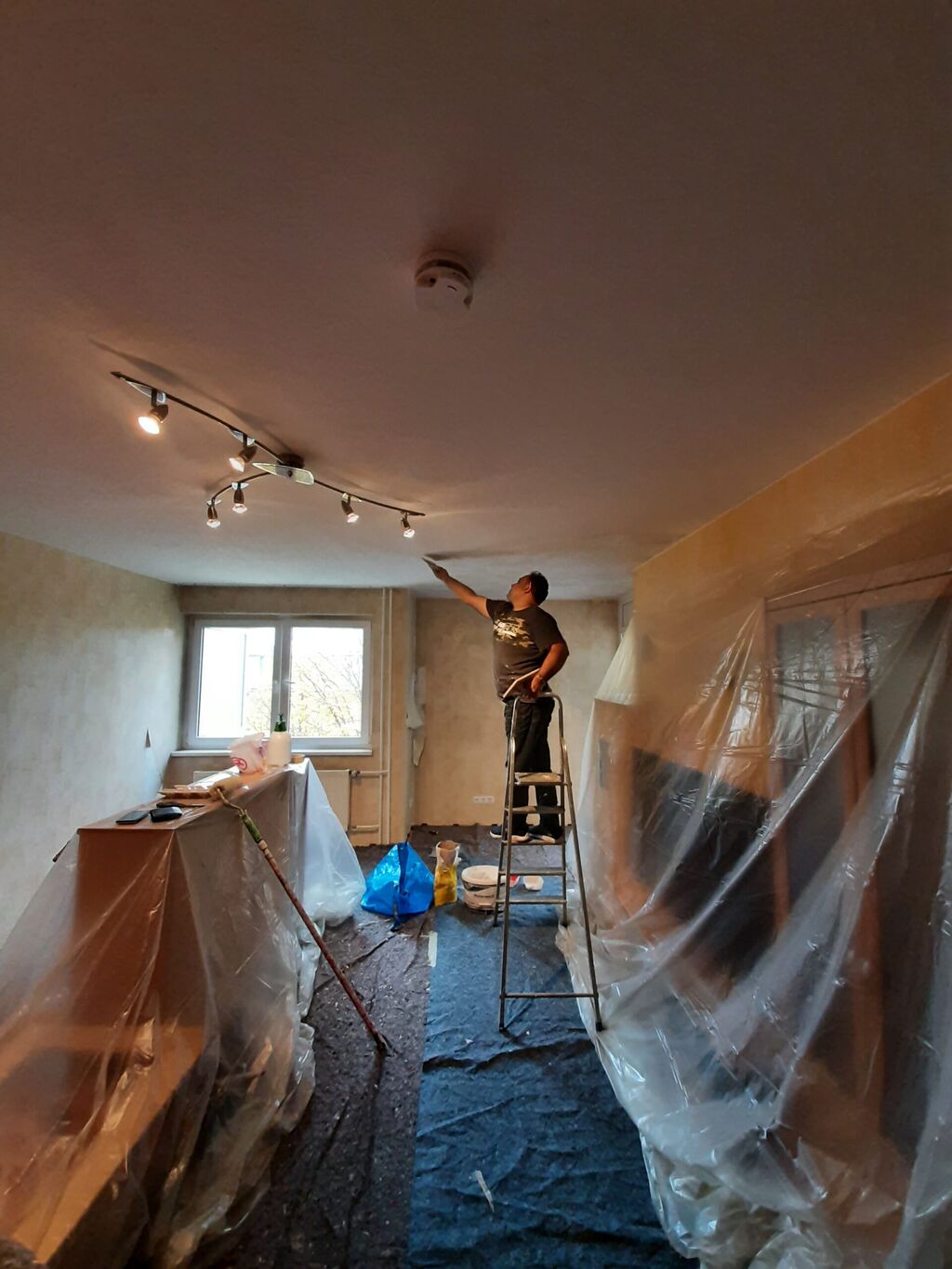 Wohnzimmer während der Arbeiten: Möbel in Folie, Decke wird gespachtelt